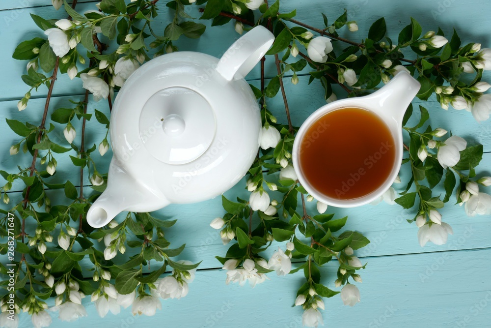 jasmine tea in a white cup, white teapot and branches of jasmine on a light blue wooden background.Organic Herbal Bio Tea jasmine tea in a white cup, white teapot and branches of jasmine on a light blue wooden background.Organic Herbal Bio Tea