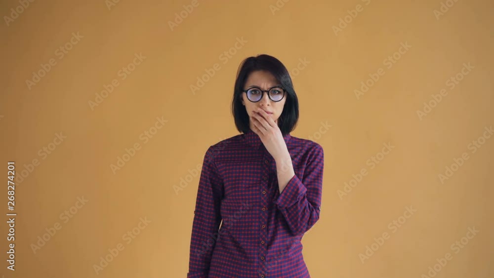 Portrait of shocked brunette in glasses feeling bad after unpleasant surprise standing on orange background. Negative emotions, fear and youth concept. Portrait of shocked brunette in glasses feeling bad after unpleasant surprise standing on orange background. Negative emotions, fear and youth concept.