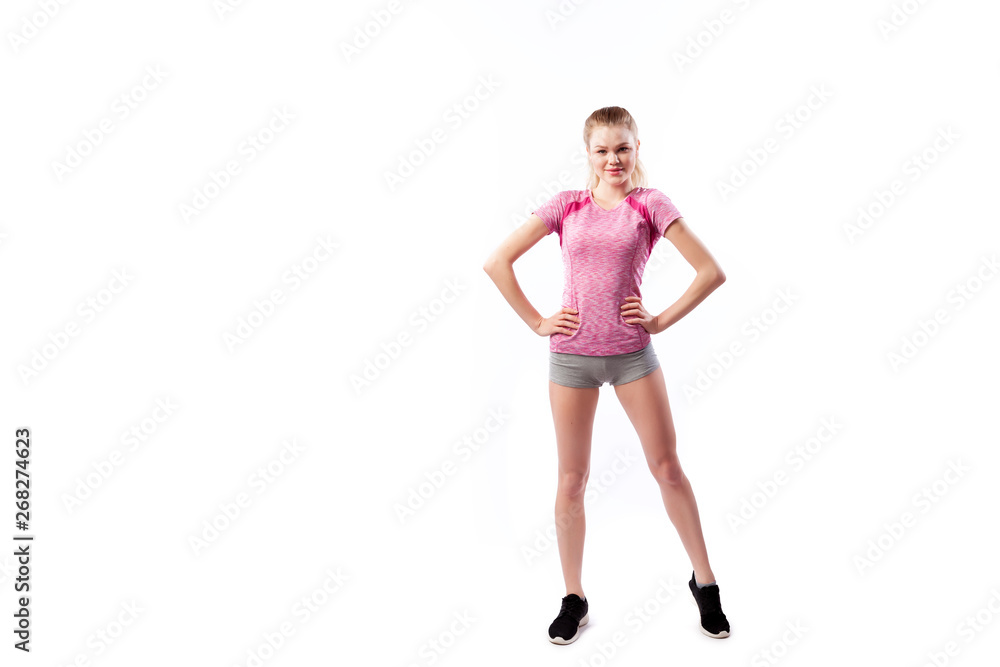 Sporty woman in t-shirt and shorts smilling, posing and holds hands on a waist on white isolated background. Photo of muscular woman in sportswear on white background. Strength and motivation. Sporty woman in t-shirt and shorts smilling, posing and holds hands on a waist on white isolated background. Photo of muscular woman in sportswear on white background. Strength and motivation.