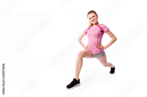 Young woman in sports clothes makes and stretch legs, doing exercise tilts, legs wide apart on white isolated background. Side view.Fit girl living an active lifestyle