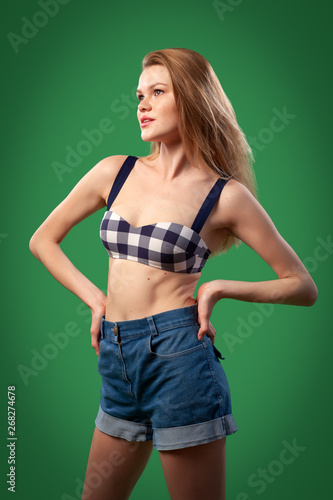 Portrait of a beautiful young  Caucasian woman 20 years old model in a black and white swimsuit and denim shorts with natural make-up posing on green isolated background