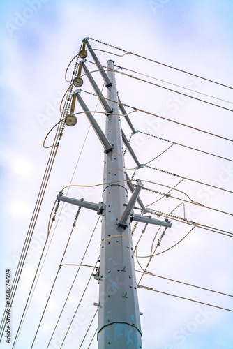 Looking up at a towering metal post supporting overhead power lines