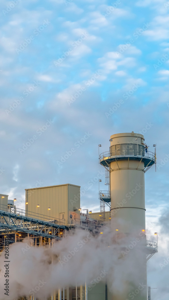 Obraz premium Vertical Cloudy blue sky viewed behind the towers and buildings of a Power Plant