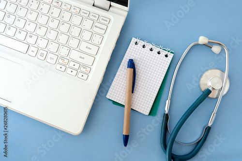 Laptop white, stethoscope, paper and pen on blue background. The concept of transition to modern equipment when recording medical records in health care facilities.