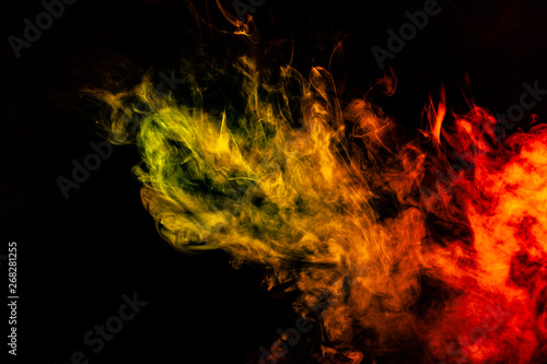 Beautiful horizontal column of smoke in the neon bright light of red  green  yellow and orange on a black background exhaled out of the vape. Nice pattern for printing and backdrop of colored waves.