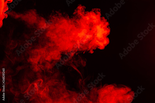 Portrait of a side mouth part of guys face with a colored backlight of monochrome smoking a vape and exhaling white red in different directions on a black isolated background. Puffs harmful to health.