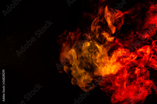 Beautiful horizontal column of smoke in the neon bright light of red, green, yellow and orange on a black background exhaled out of the vape. Nice pattern for printing and backdrop of colored waves.