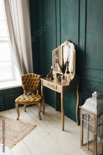 beautiful luxury vintage colorful interior. classic room with wooden floor green walls with moldings, dressing golden  table with mirror decorated with elements, yellow chair 