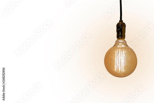 An old vintage light bulb on white background. Old shining glass bulb with orange and yellow light. Space for copy. Light bulb on a wire.