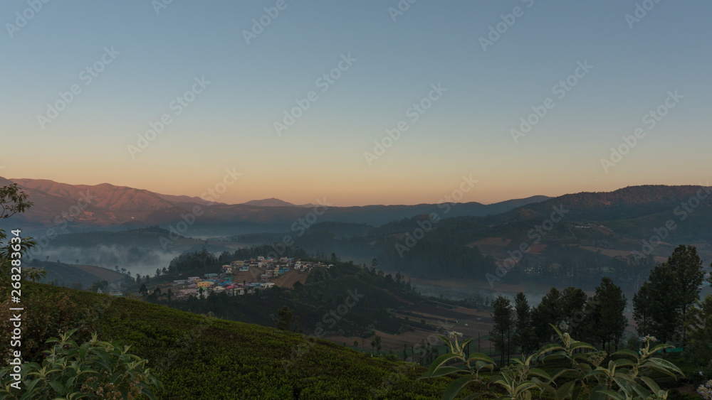 dramatic sunrise over the Emerald lake in Ooty with mountains in the background and mist covering the lake on a cold early morning, India. Top view of Emerald lake and village.