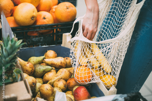 Woman with mesh bag full of fresh vegetables shopping at the store, zero waste concept