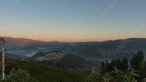 dramatic sunrise over the Emerald lake in Ooty with mountains in the background and mist covering the lake on a cold early morning  India. Top view of Emerald lake and village.
