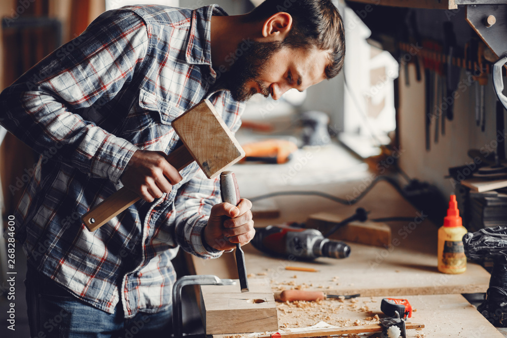 A man carves a tree. The carpenter works with a hammer in a studio. An engineer provides a tree shape