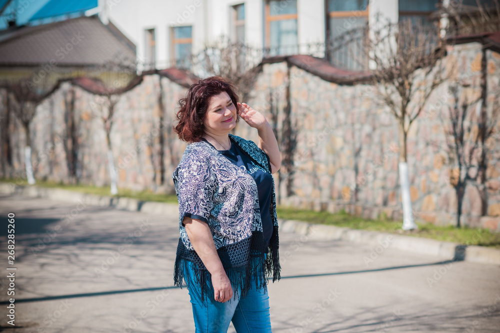 Woman of plus size, American or European appearance walks in the city enjoying life. Middle age lady with excess weight, stylishly dressed at the city park .Natural beauty 