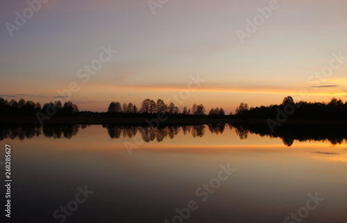 Beautiful sunset on the forest lake. The sun is reflected in the water. Bright contrasting sky.