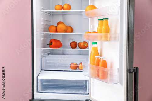 Modern fridge with fresh products on color background, closeup