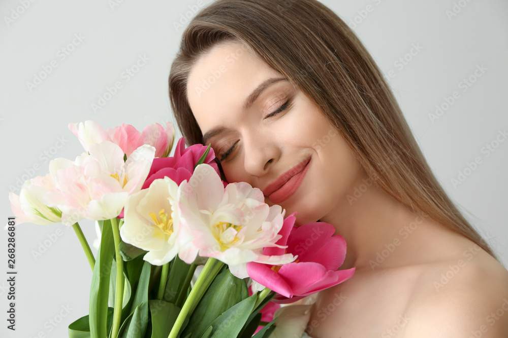 Young woman with bouquet of beautiful tulips on light background