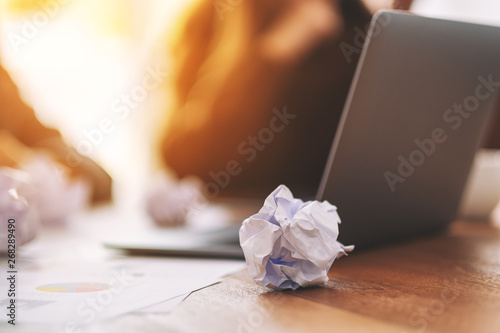 Fotografie Closeup image of screwed up papers and laptop on wooden table in office