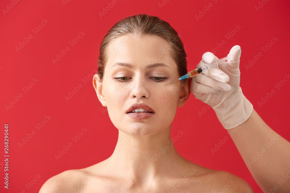 Hand of plastic surgeon with syringe and young woman against color background Hand of plastic surgeon with syringe and young woman against color background