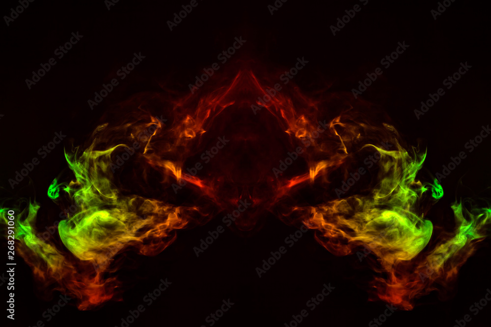 Fototapeta premium Abstract image of smoke of different green, yellow, orange and red colors in the form of horror in the shape of the head, face and eye on a black isolated background. Soul and ghost in mystical symbol