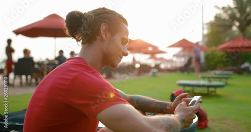 Young attractive man uses smartphone while sitting on the beach. in slow motion. Shot on Canon 1DX mark2 4K camera photo