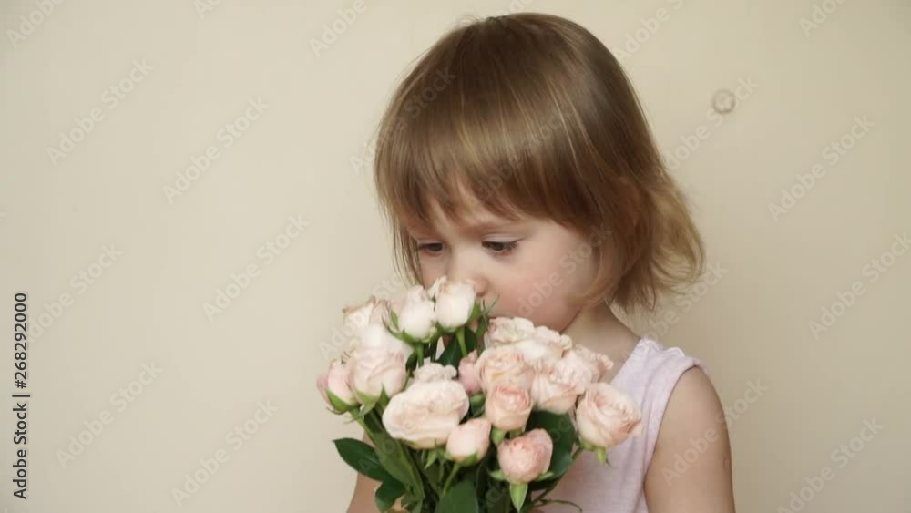 Little caucasian cute blonde girl stands and holds bouquet of tea roses. Child smells flowers and smiles Little caucasian cute blonde girl stands and holds bouquet of tea roses. Child smells flowers and smiles