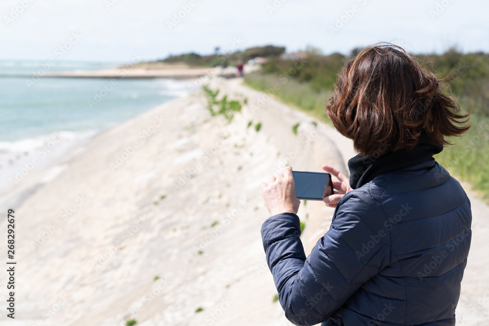 brunette woman standing with smart phone on a beach in tourist concept