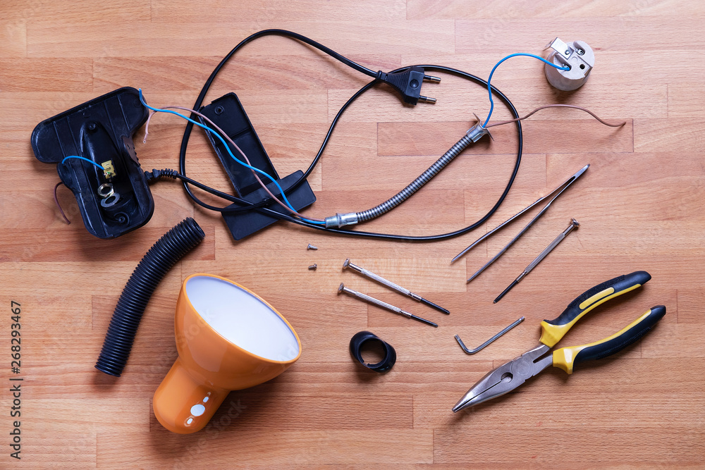 Broken desk lamp details and instruments top view. Technician, electrician service workplace chaos concept. Work instruments on table, wooden floor. Electronics fixing, repairing. Pliers and nails Broken desk lamp details and instruments top view. Technician, electrician service workplace chaos concept. Work instruments on table, wooden floor. Electronics fixing, repairing. Pliers and nails