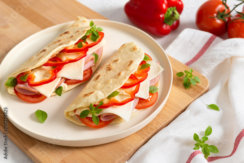 Italian piadina on a white plate with vegetables tomatoes and pepper on white background. Italian cuisine. Side view, copy space.