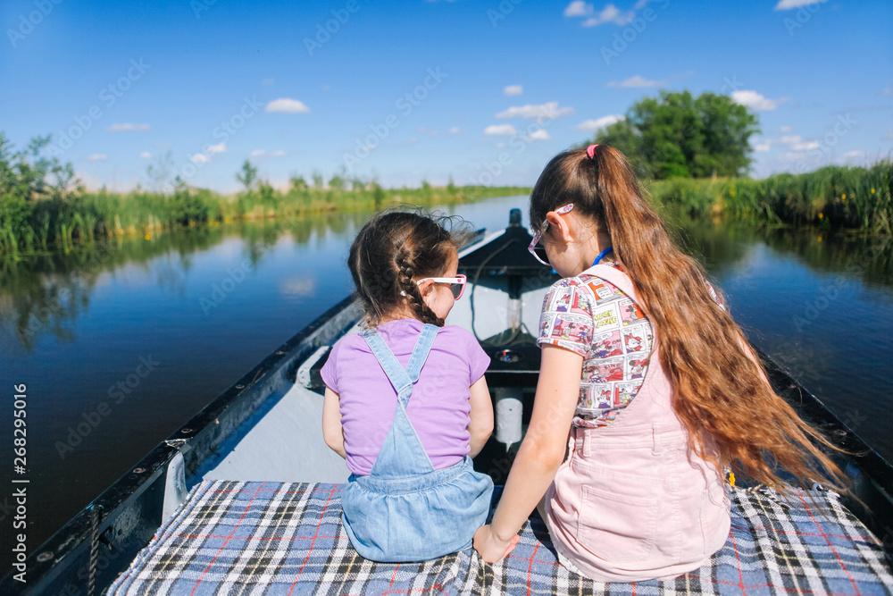Back view of happy two girl with long hair sit on a boat ride at the river. Enjoying a lovely summer day.