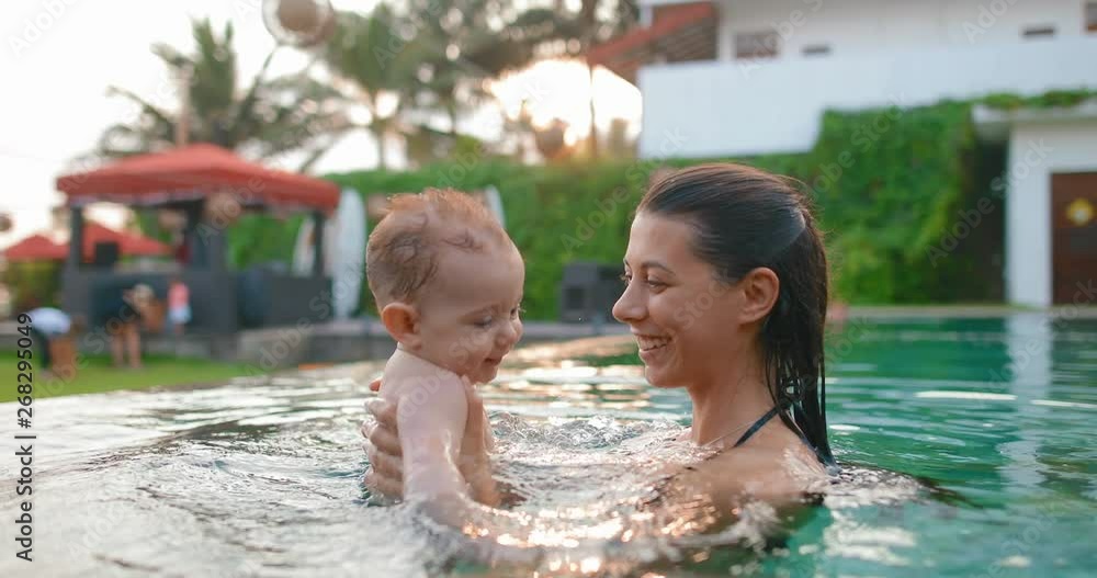 Young mother with 8 month old son in pool. Baby likes to swim, he slaps his hands on the water and laughs. in slow motion. Shot on Canon 1DX mark2 4K camera Young mother with 8 month old son in pool. Baby likes to swim, he slaps his hands on the water and laughs. in slow motion. Shot on Canon 1DX mark2 4K camera