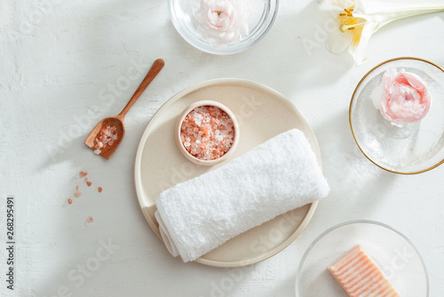 Top view of Spa products with towel and oil on plate, flowers, soap on white background