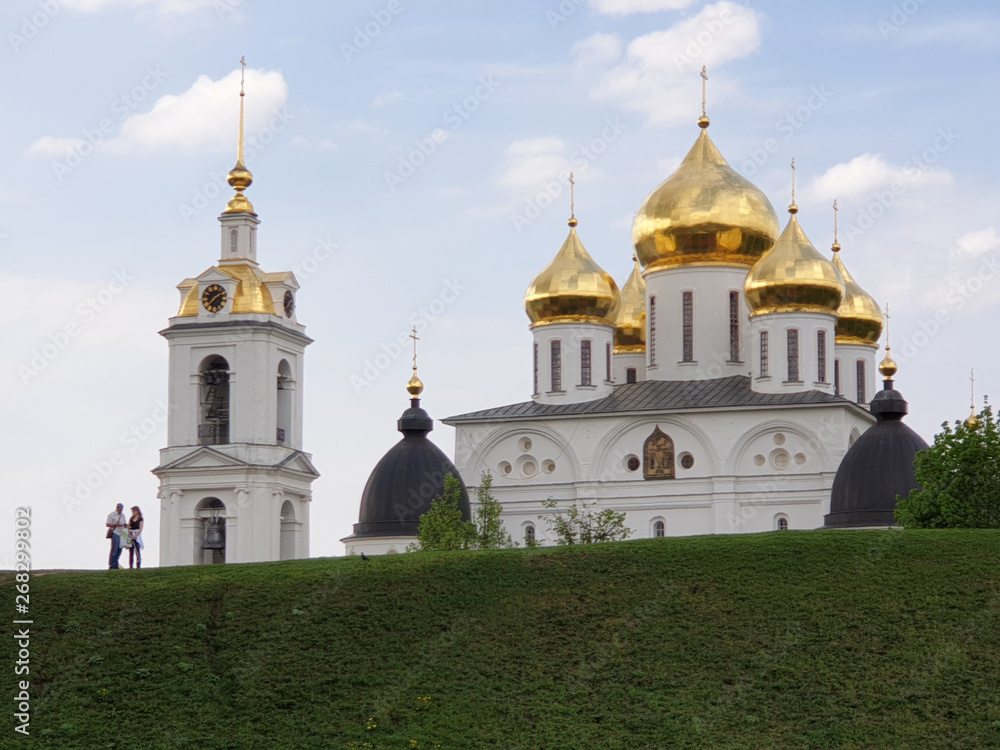 Dmitrov Kremlin. Tourists man and woman studying the map against a clear sky, a beautiful white Orthodox Church with Golden domes and a bell tower in summer on a clear Sunny day