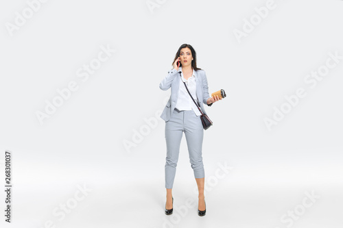 Another minute and you're fired. Young woman in gray suit is getting shocking news from boss or colleagues. Looking numbed while dropping coffee. Concept of office worker's troubles, business, stress.