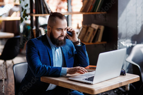 young bearded businessman at work in the office. A man sits at a laptop talking through a mobile phone. telephone conversations in coworking