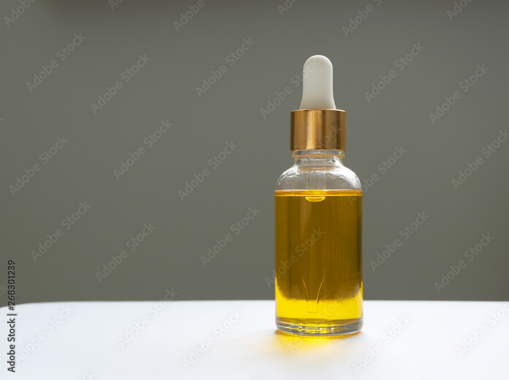 Oil serum in glass bottle with pipette. Yellow essence on gray background Oil serum in glass bottle with pipette. Yellow essence on gray background
