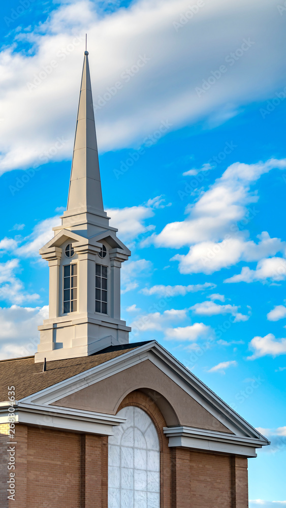 Vertical Exterior of a beautiful church with a white steeple against cloudy blue sky Vertical Exterior of a beautiful church with a white steeple against cloudy blue sky
