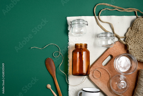 Zero waste concept. Reusable, recycled, homemade produce bag for fruit or vegetables, linen tablecloth, glass jar, cup and wooden spoons on green background.