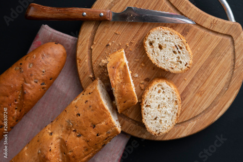 sliced french baguette on a wooden board, bread knife laying around, dark backgrounds
