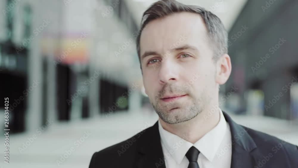 Close-up head and shoulders shot of middle aged businessman in formal suit walking along hall in office center Close-up head and shoulders shot of middle aged businessman in formal suit walking along hall in office center