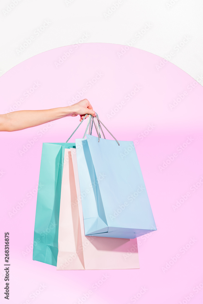 cropped view of young woman holding colorful shopping bags on white with pink circle