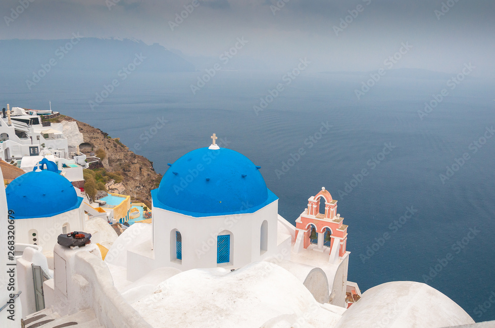 Blue dome and rose bell tower in the village of Oia on a rare rainy day