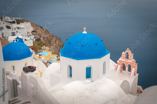 Tilt shift effect of blue dome and rose bell tower in the village of Oia