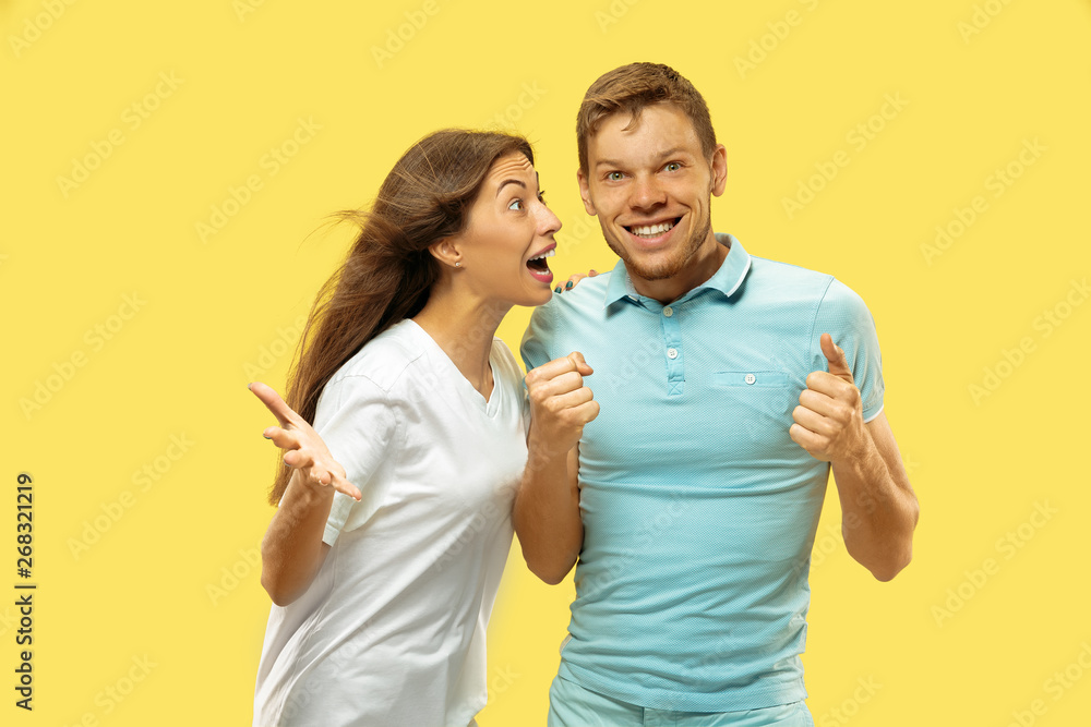Naklejka premium Beautiful young couple's half-length portrait on yellow studio background. Woman and man in shirts celebrating and showing the sign of OK. Facial expression, human emotions concept. Trendy colors.