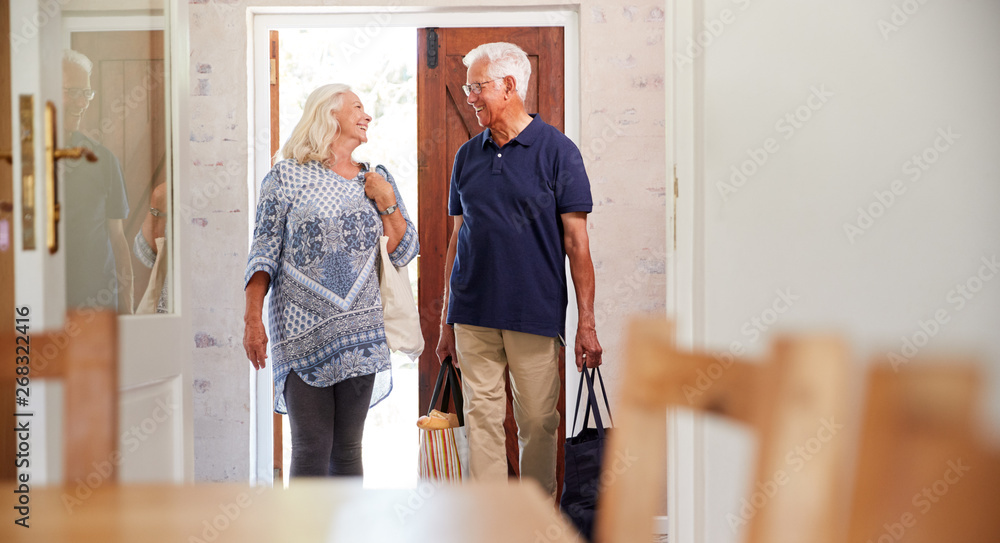Fototapeta premium Senior Couple Returning Home From Shopping Trip Carrying Grocery Bags Through Kitchen