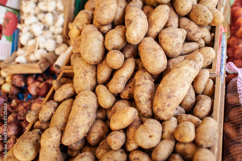 A closeup of potatoes of different shapes and sizes in wooden boxes. There are other vegetables like onions and garlic on the blurred background A closeup of potatoes of different shapes and sizes in wooden boxes. There are other vegetables like onions and garlic on the blurred background