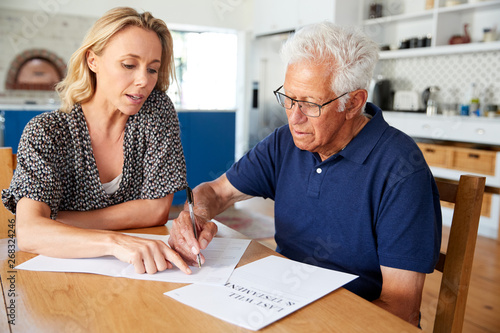 Woman Helping Senior Man To Complete Last Will And Testament At Home photo
