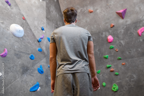 fitness, extreme sport, bouldering, people and healthy lifestyle concept - young man at indoor climbing wall in gym from back