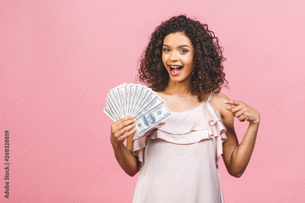 Rich girl! Money winner! Surprised beautiful african american woman in dress holding money and looking at the camera isolated against pink background. Rich girl! Money winner! Surprised beautiful african american woman in dress holding money and looking at the camera isolated against pink background.
