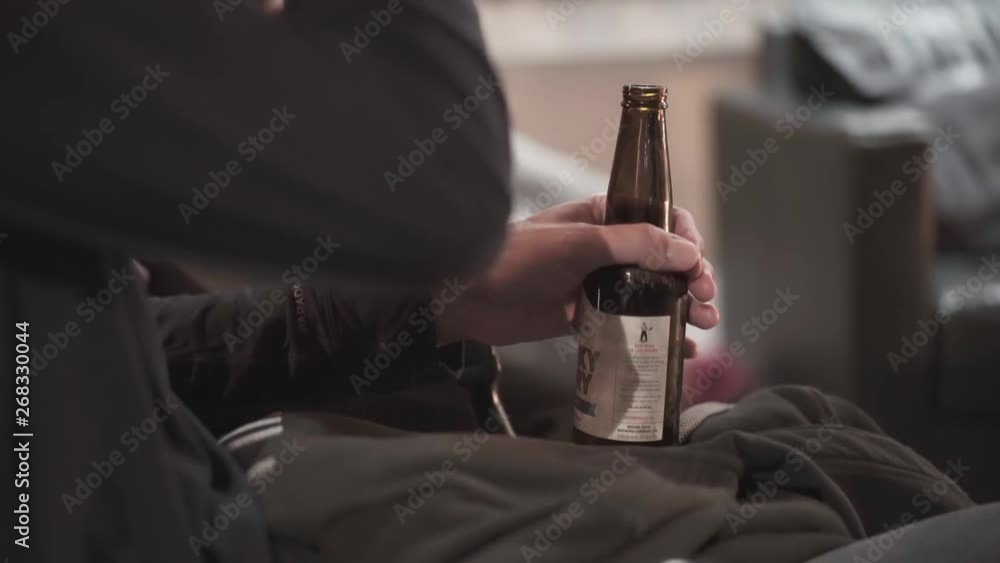 Close-up shot of an arm of a man holding a bottle of beer while having a conversation with some other people. Close-up shot of an arm of a man holding a bottle of beer while having a conversation with some other people.